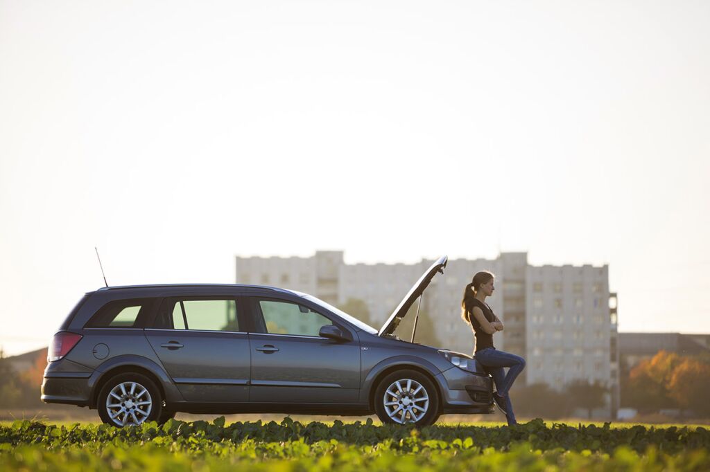 Woman Waiting On Front Bumper During Roadside Assistance Call